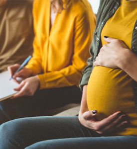 surrogate touching pregnancy bump while sitting next to intended parents discussing U.S. surrogacy and surrogate compensation