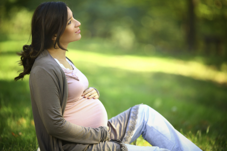 Surrogate sitting on grass holding her pregnant belly thinking about common disqualifiers