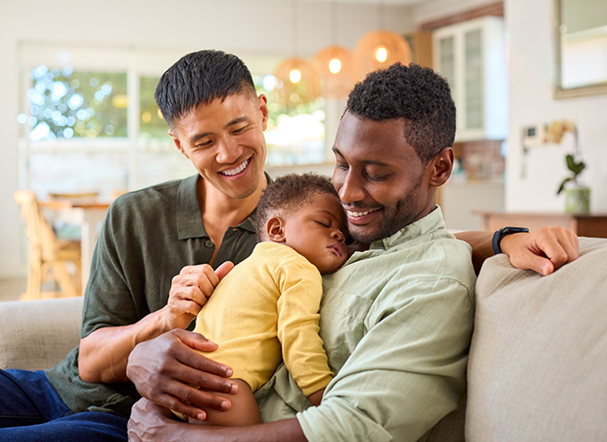 Male couple sitting on couch holding their baby